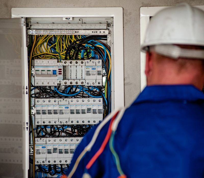 electrician watching towards switchboard with wires on shoulder