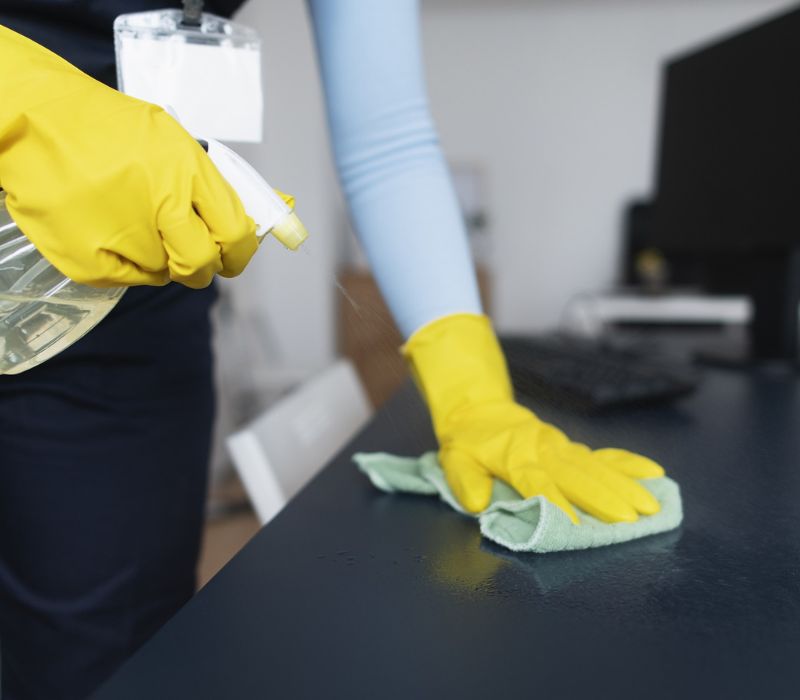 someone cleaning office desk with spray and cloth